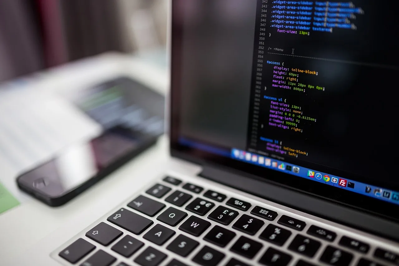 Ordinateur portable affichant du code source, smartphone et clavier mécanique sur un bureau de travail
